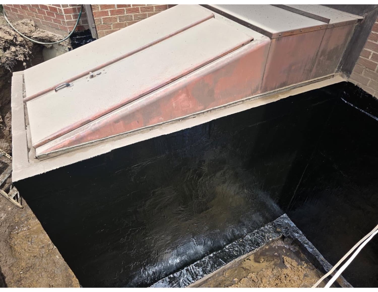 Exterior basement wall and Bilco bulkhead entrance sealed with black rubberized waterproofing membrane after excavation in Western PA