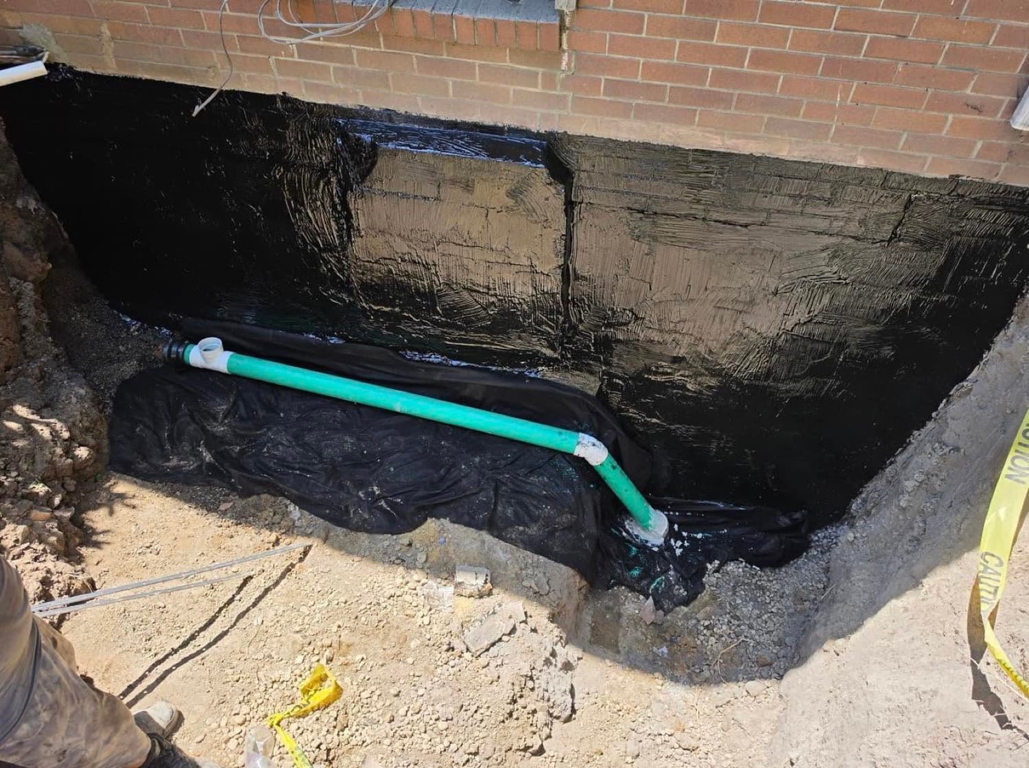 Finished exterior rubberized waterproofing membrane on a foundation wall with a new footer drain line and filter fabric before backfill