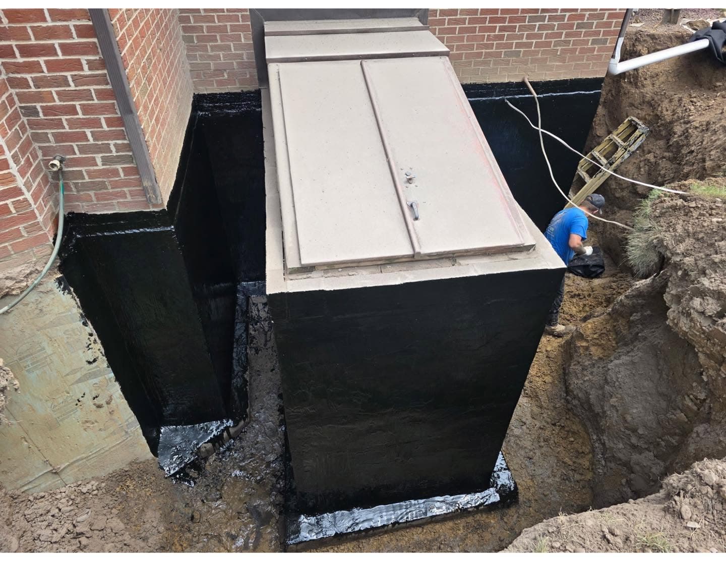 Exterior basement waterproofing dig-out on a brick home in Western PA, foundation excavated and sealed with a black Tremco waterproof coating