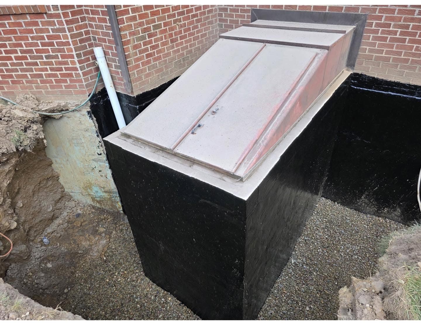 Completed exterior basement waterproofing around a bulkhead entry, foundation sealed and backfilled, Western PA