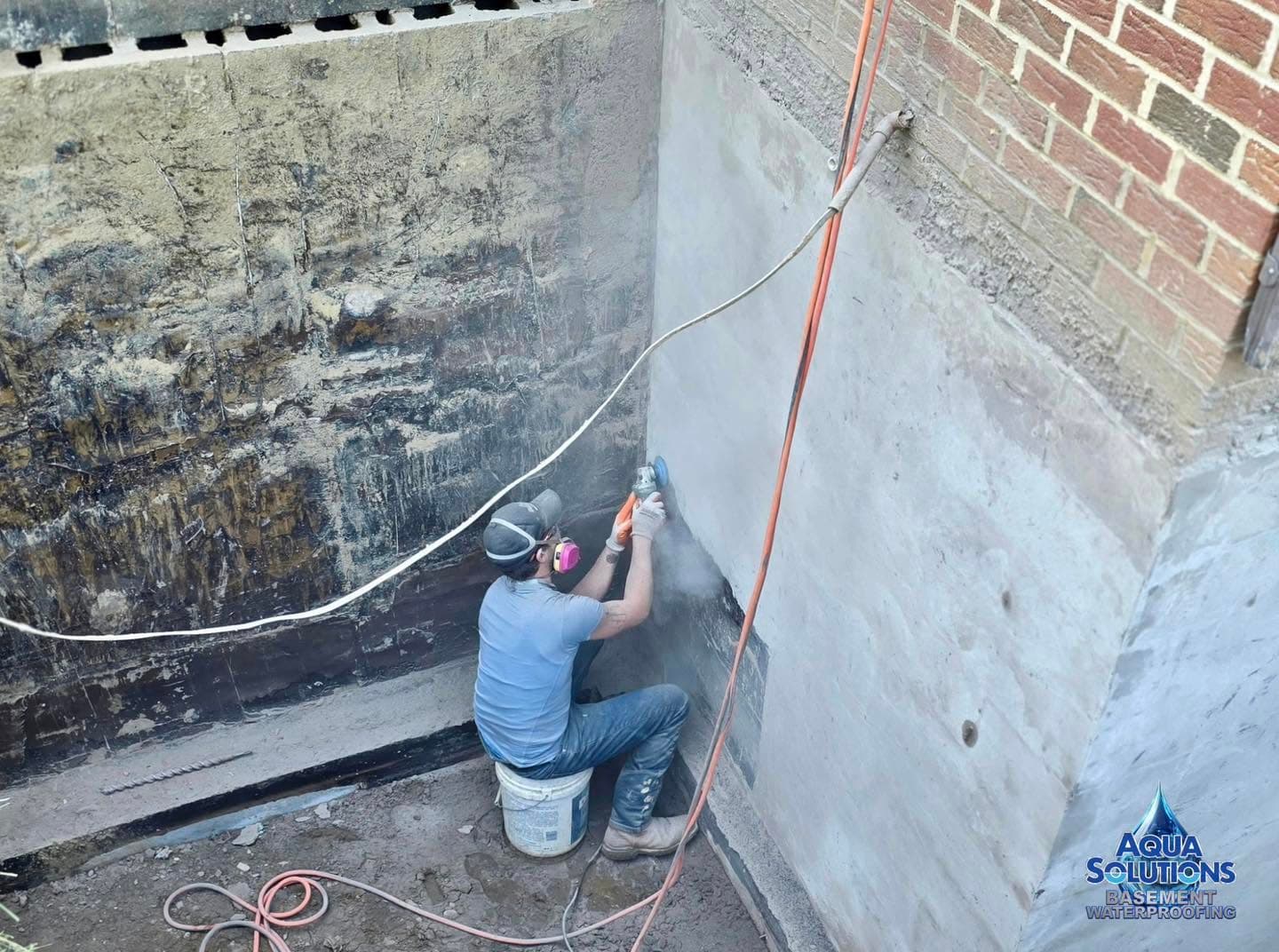 Aqua Solutions technician grinding and prepping a foundation wall before applying exterior waterproofing sealant in Western PA
