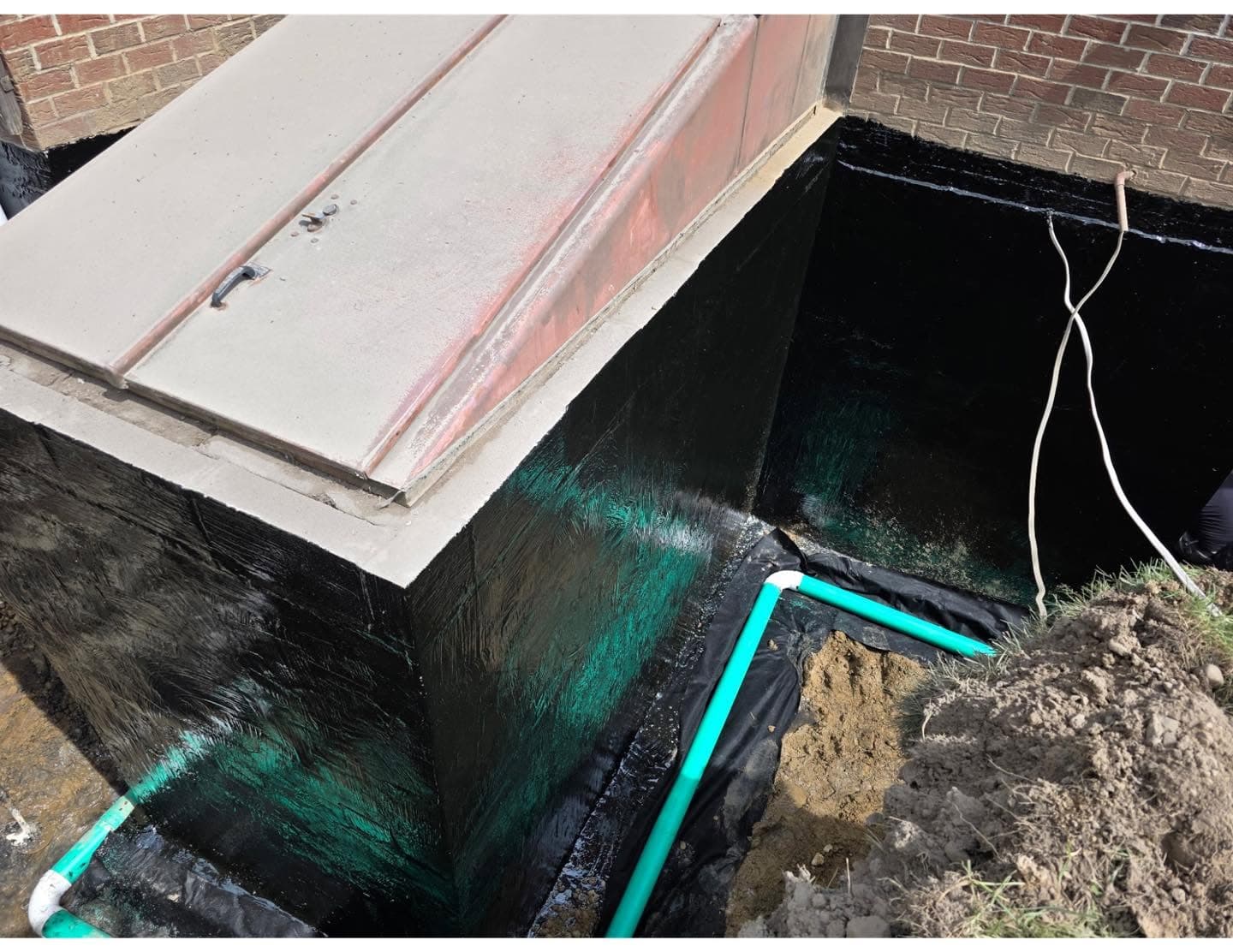Exterior foundation wall sealed with Tremco coating and membrane beside a bulkhead, perimeter footer drain being installed, Western PA
